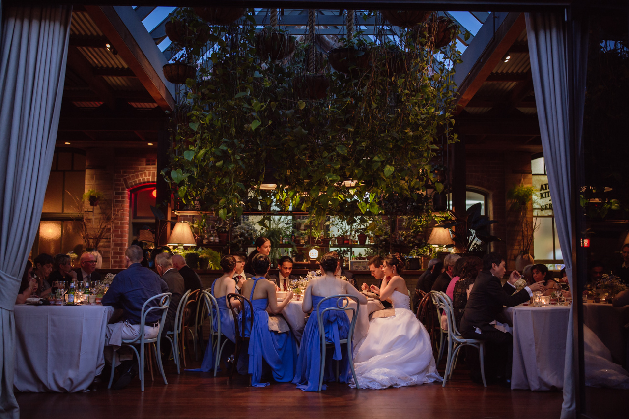 A view inside a wedding reception venue. The bridal party can be seen centre of frame