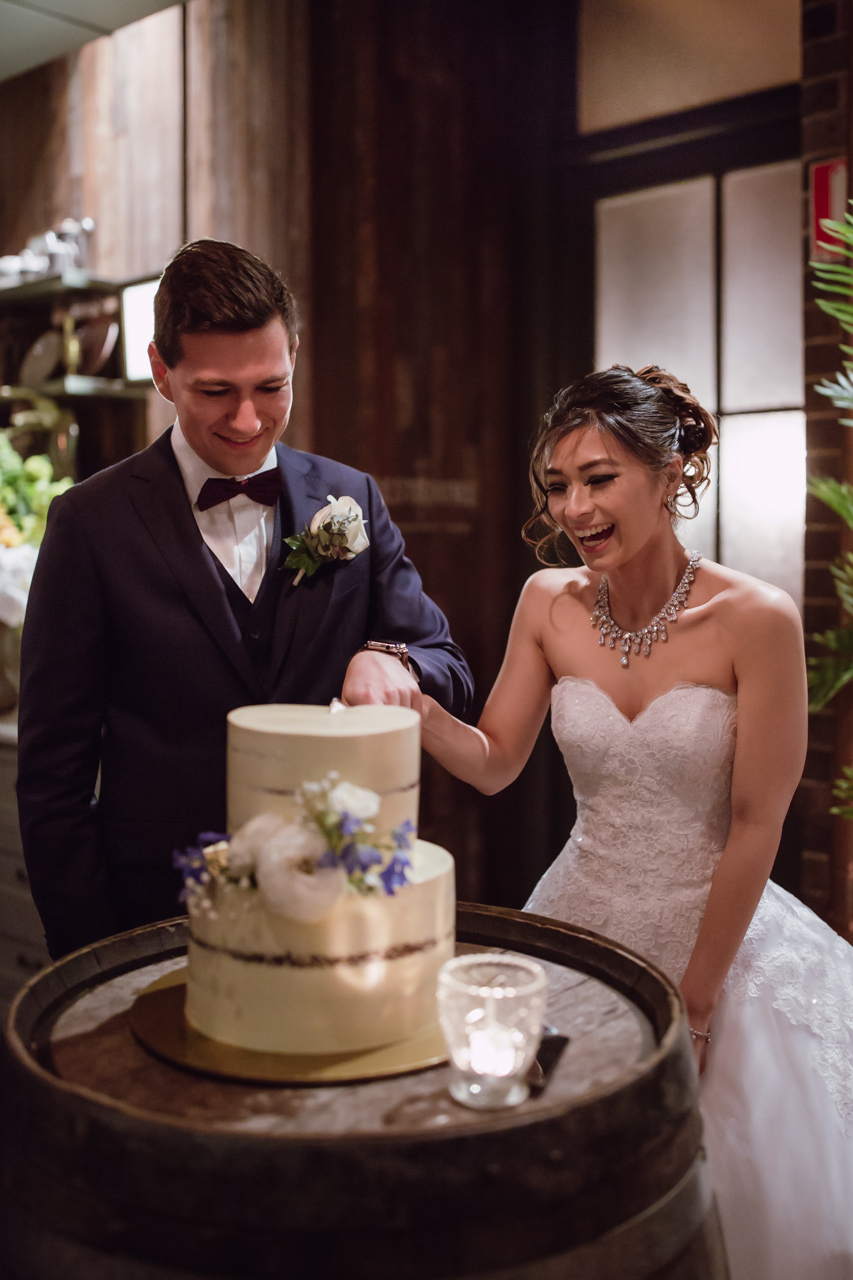 A man and woman smiling as they cut a wedding cake