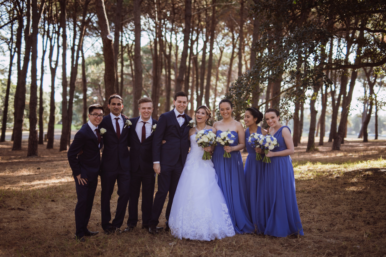 A bride and groom and bridal party standing close together and smiling/laughing