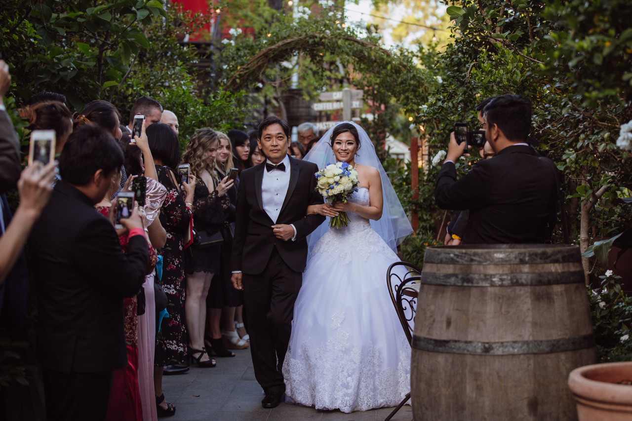 A bride linking arms with her dad as she walks down the aisle in a garden setting