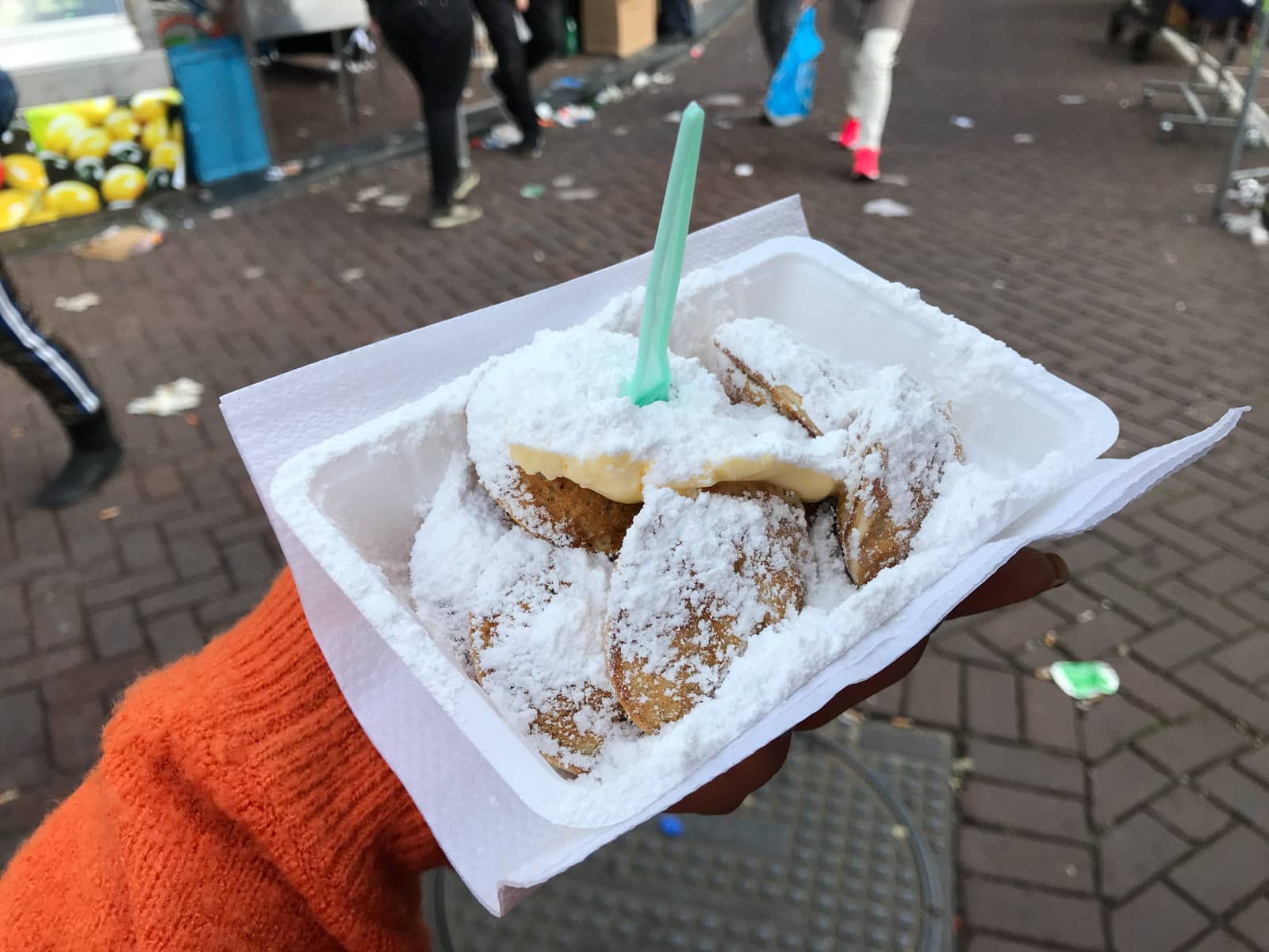 A close up of a paper tray of poffertjes (Dutch mini pancakes) doused with powdered sugar