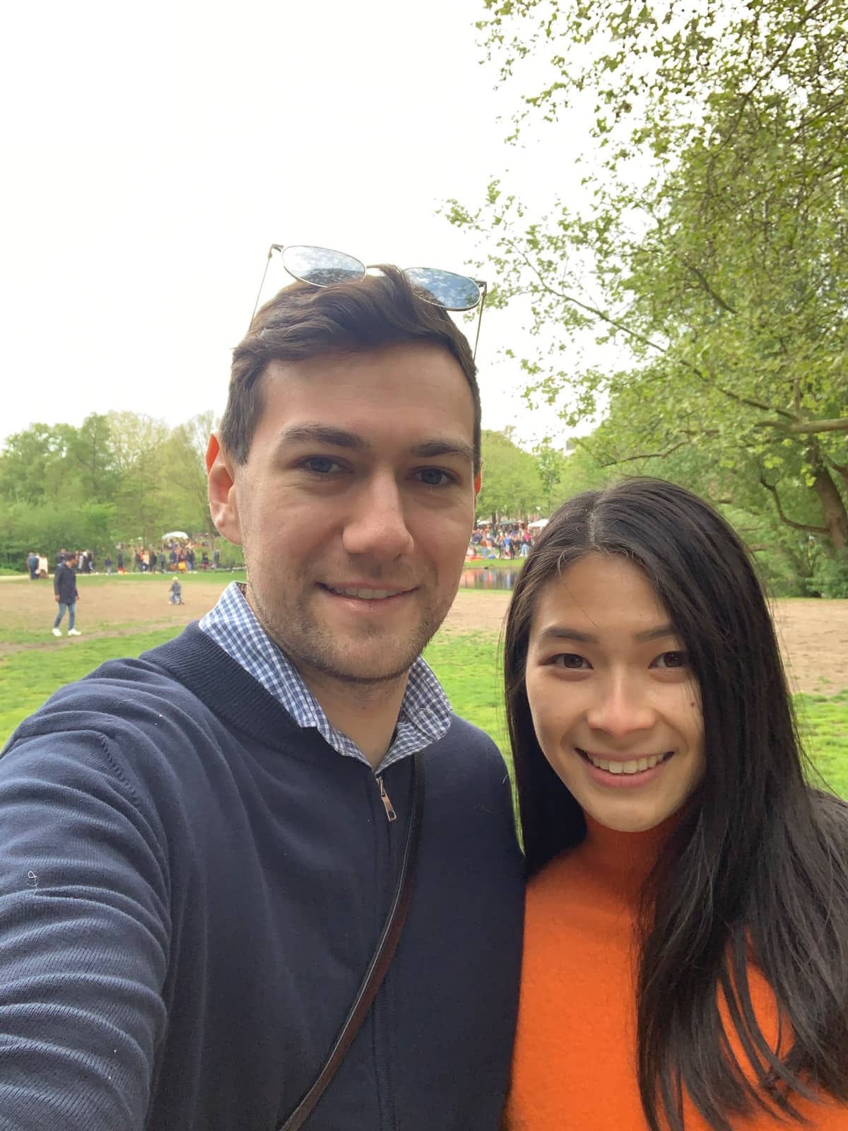 A man in a dark jacket and dark hair, and a woman in an orange turtleneck sweater, smiling for a selfie