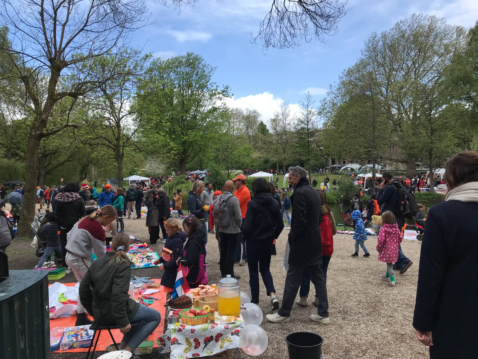The entrance of a small park that is busy with people, some selling second hand goods and toys in stalls on the sides of the path