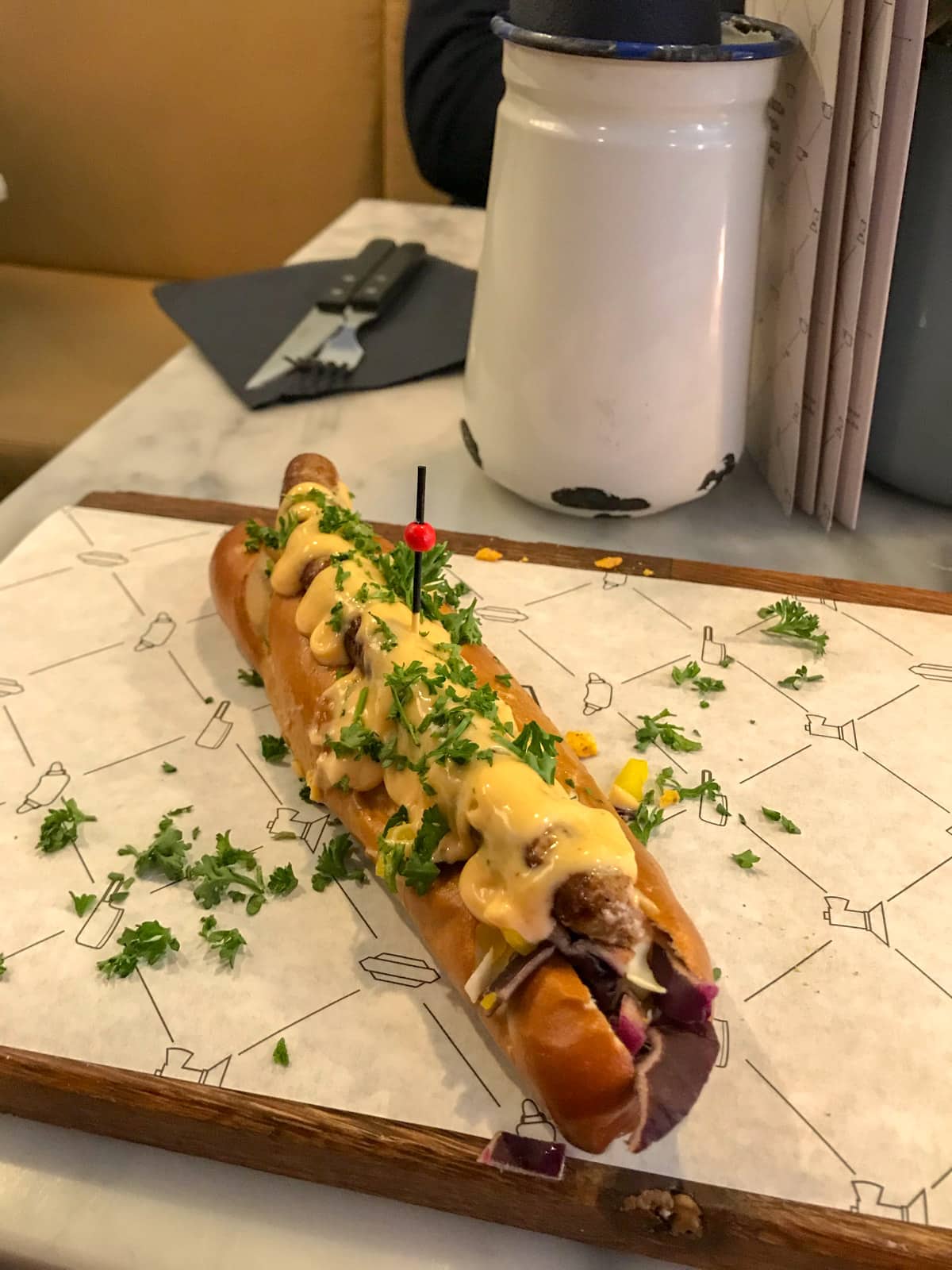 A small hot dog with mustard sauce and sprinkled herbs on a serving board