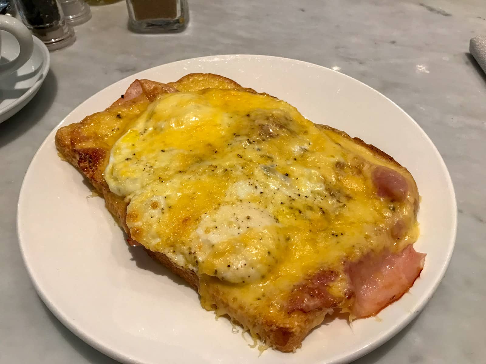 A white plate with fried eggs, cheese and ham toasted on it.