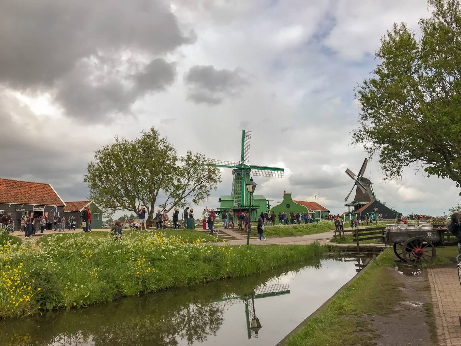 A couple of windmills seen over a dirty moat, in a small village. The sky is very cloudy and grey.