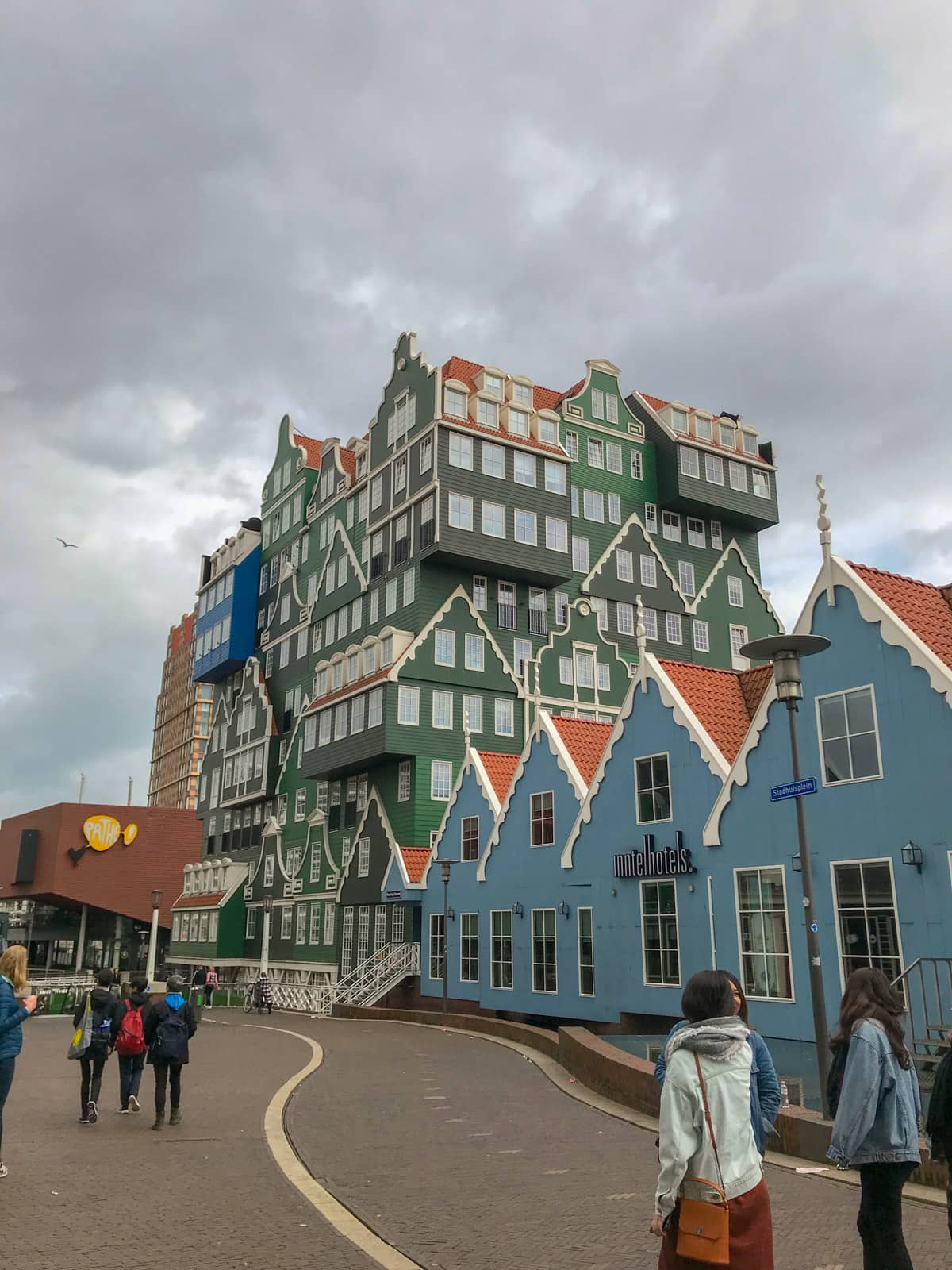 An interestingly-architectured building resembling little houses put together, in colours of green, blue, and blue-grey. The sky is very grey.