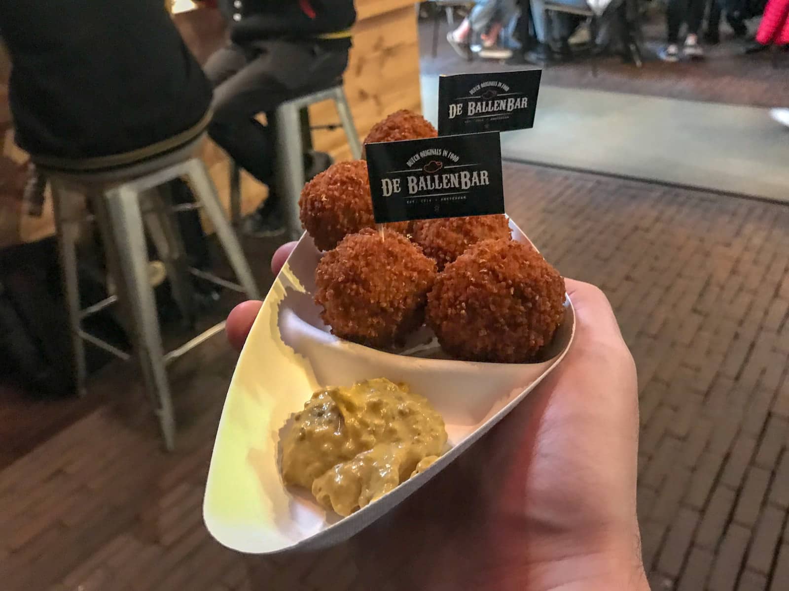 Dutch bitterballen in a cardboard tray with sauce in a small compartment of the tray. A man is holding the tray in his hand