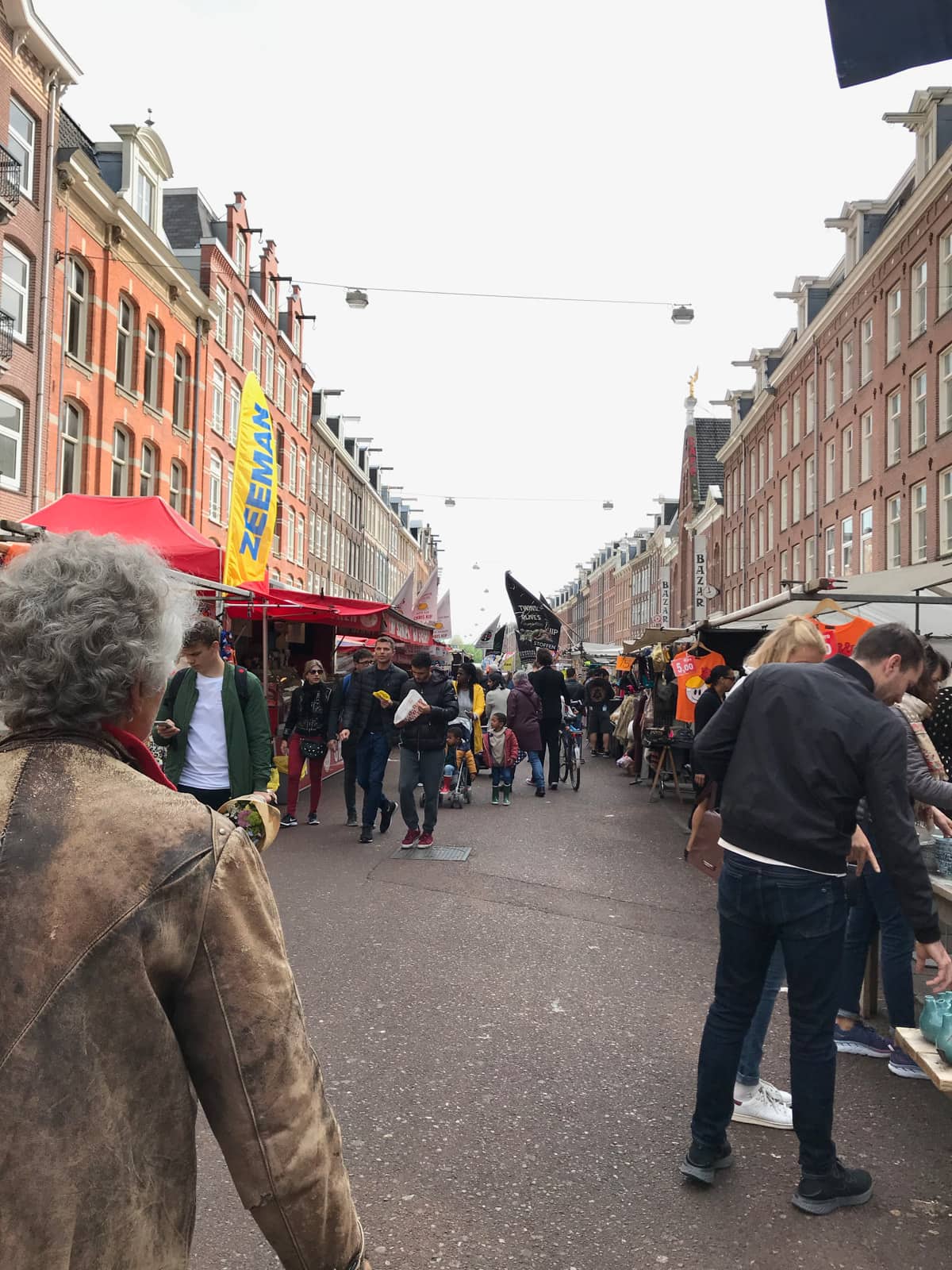 A street market seen from the middle, with stalls lining the sides. The market is not that busy but there are some people walking through it