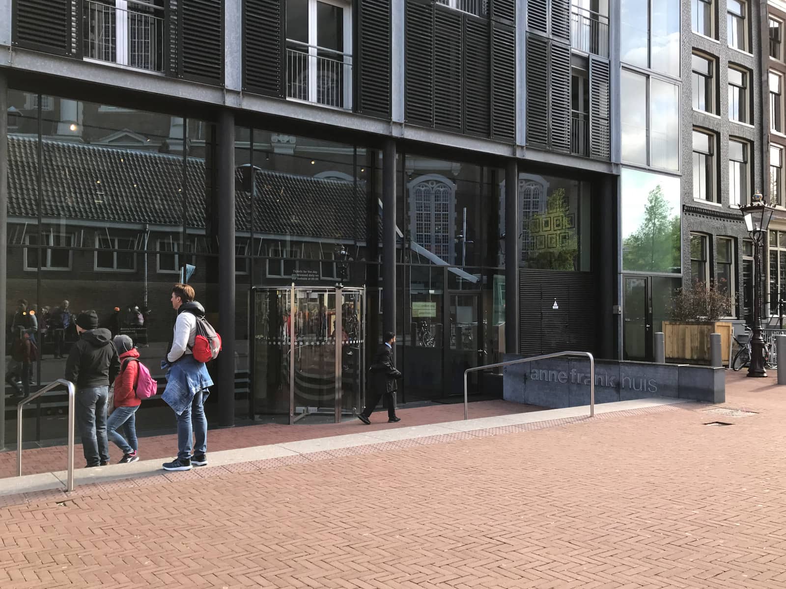 The front of the Anne Frank House – a dark, subtle building with tinted glass windows. Some people stand around its entrance