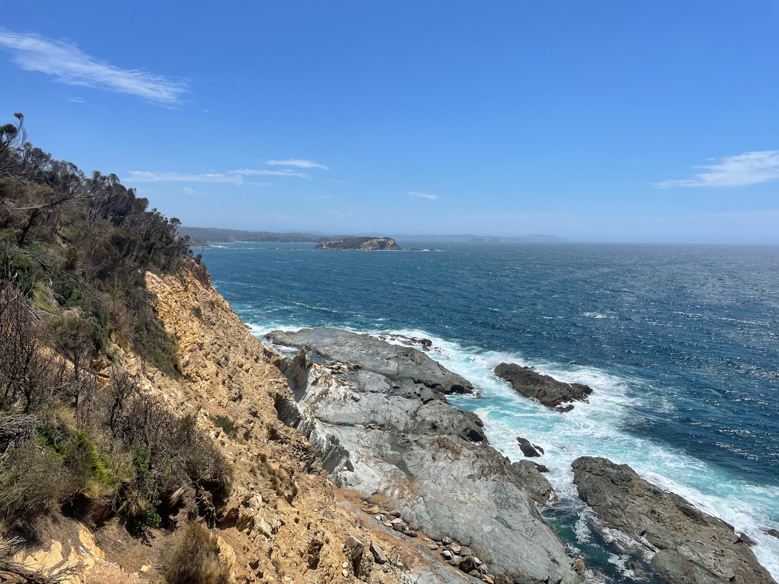 A view of the deep blue ocean with a cliff face in the foreground, of both an earthy yellow colour and a grey colour