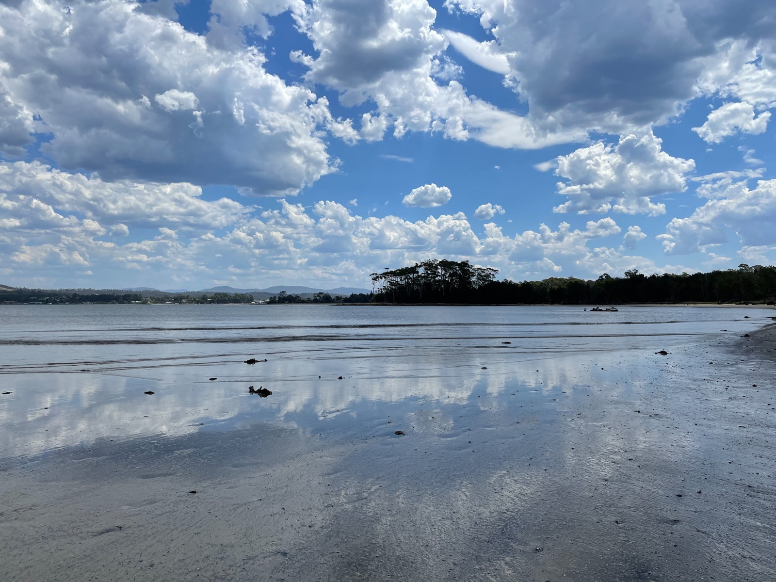 A very shallow and uneven body of water. The cloudy sky creates reflections in the water. Some trees can be seen in the background but look dark like shadows.