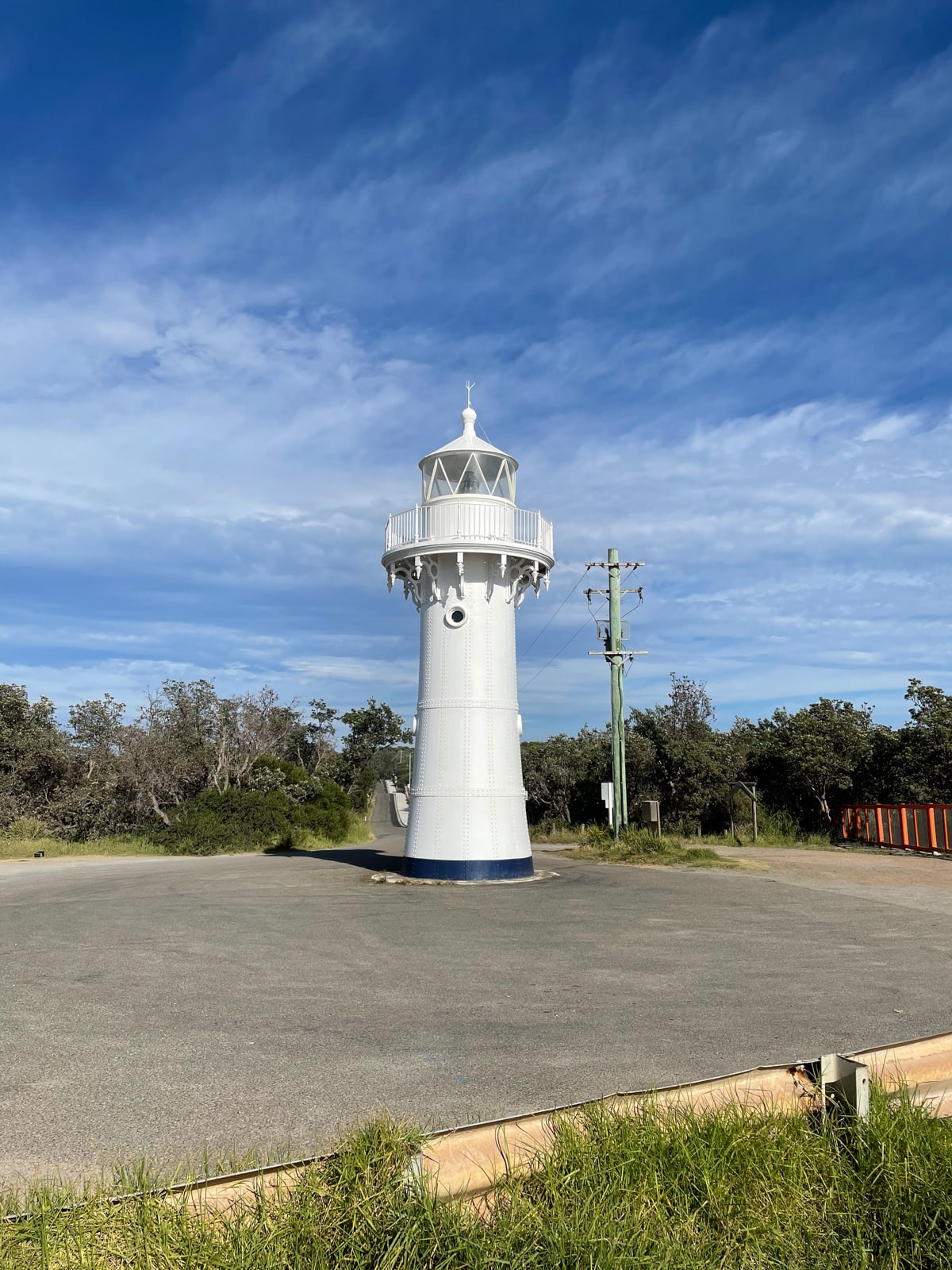 A white lighthouse in the middle of a dead-end road. The sky in the background is blue with streaks of clouds.