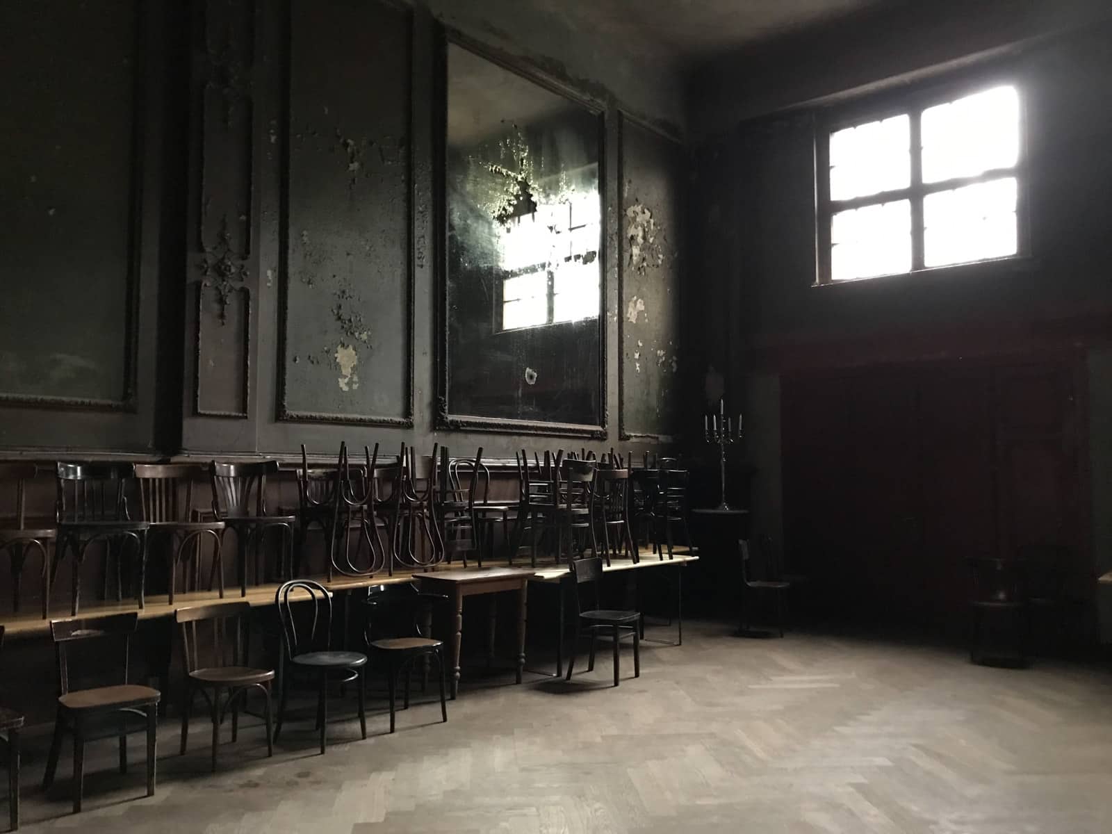 The dark interior of an old ballroom with stacks of chairs on the sides, old mirrors on the walls