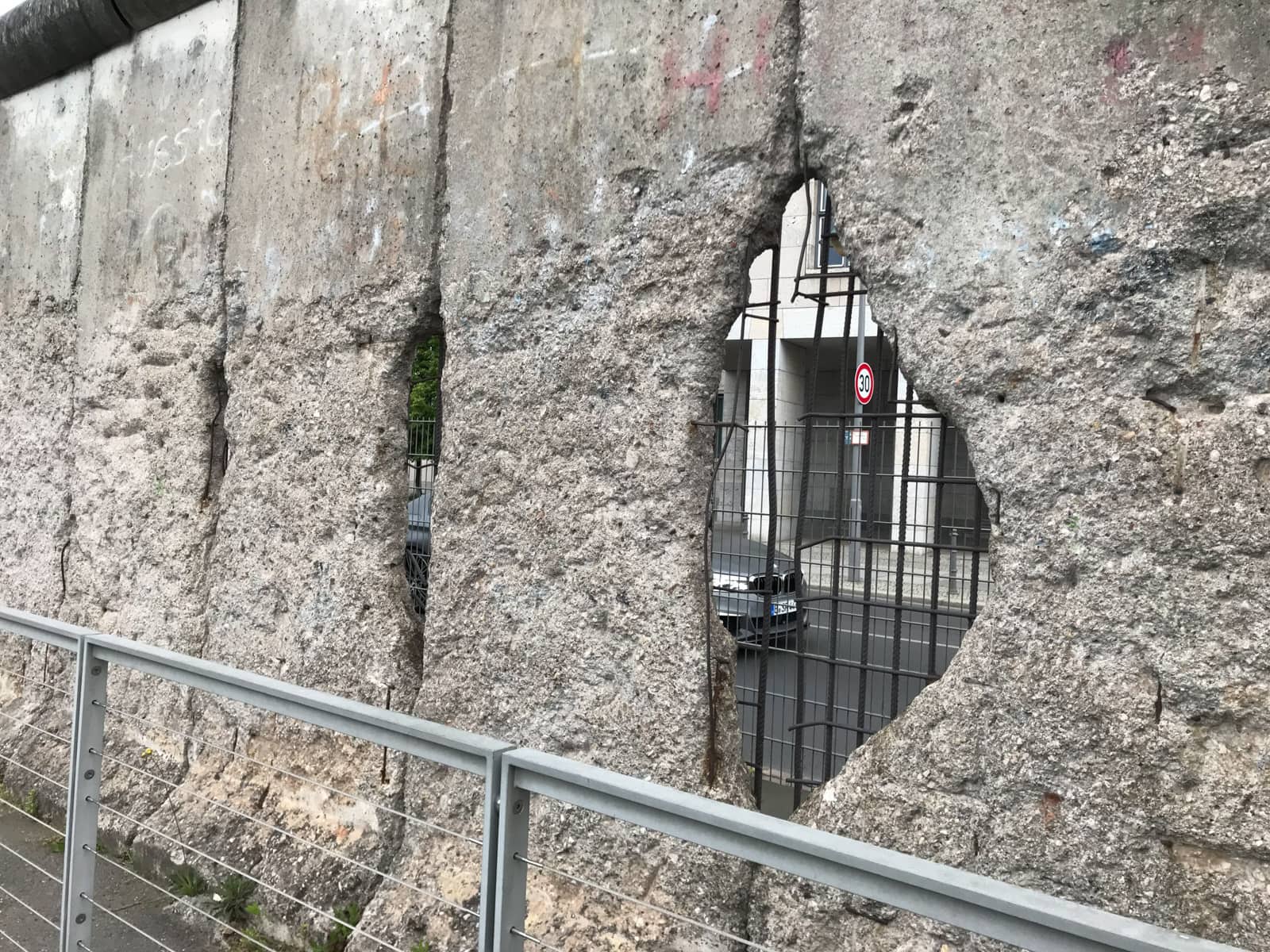 A part of the Berlin Wall, made of concrete, with a hole in it showing the interior of the wall being made of criss-crossed metal