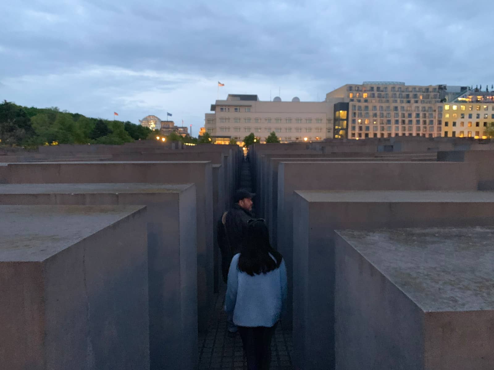 A man, and a woman walking behind him, walking through large pillars of a memorial at dusk