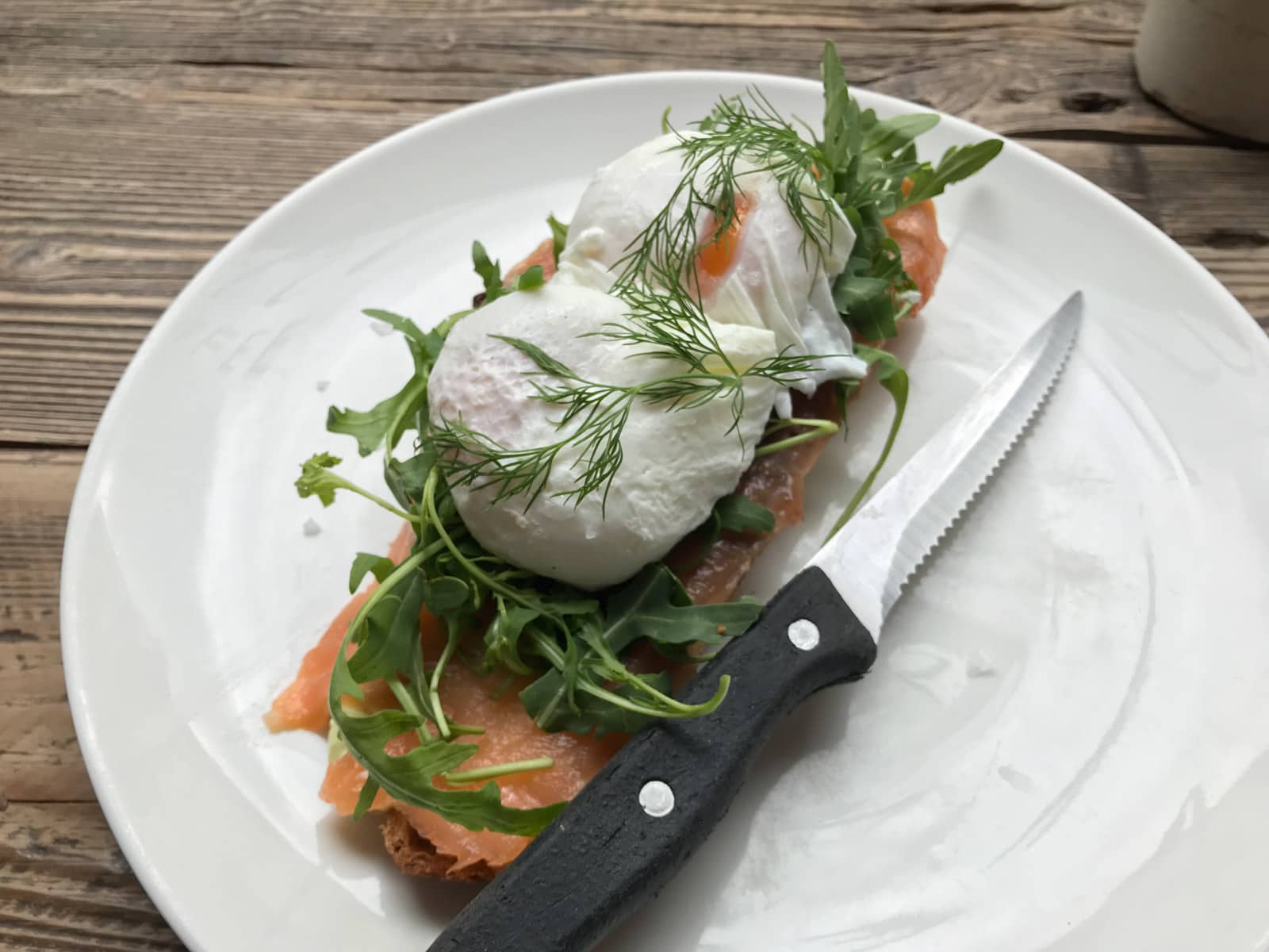 A white plate with smoked salmon and poached eggs on toast, with a serrated knife next to the food