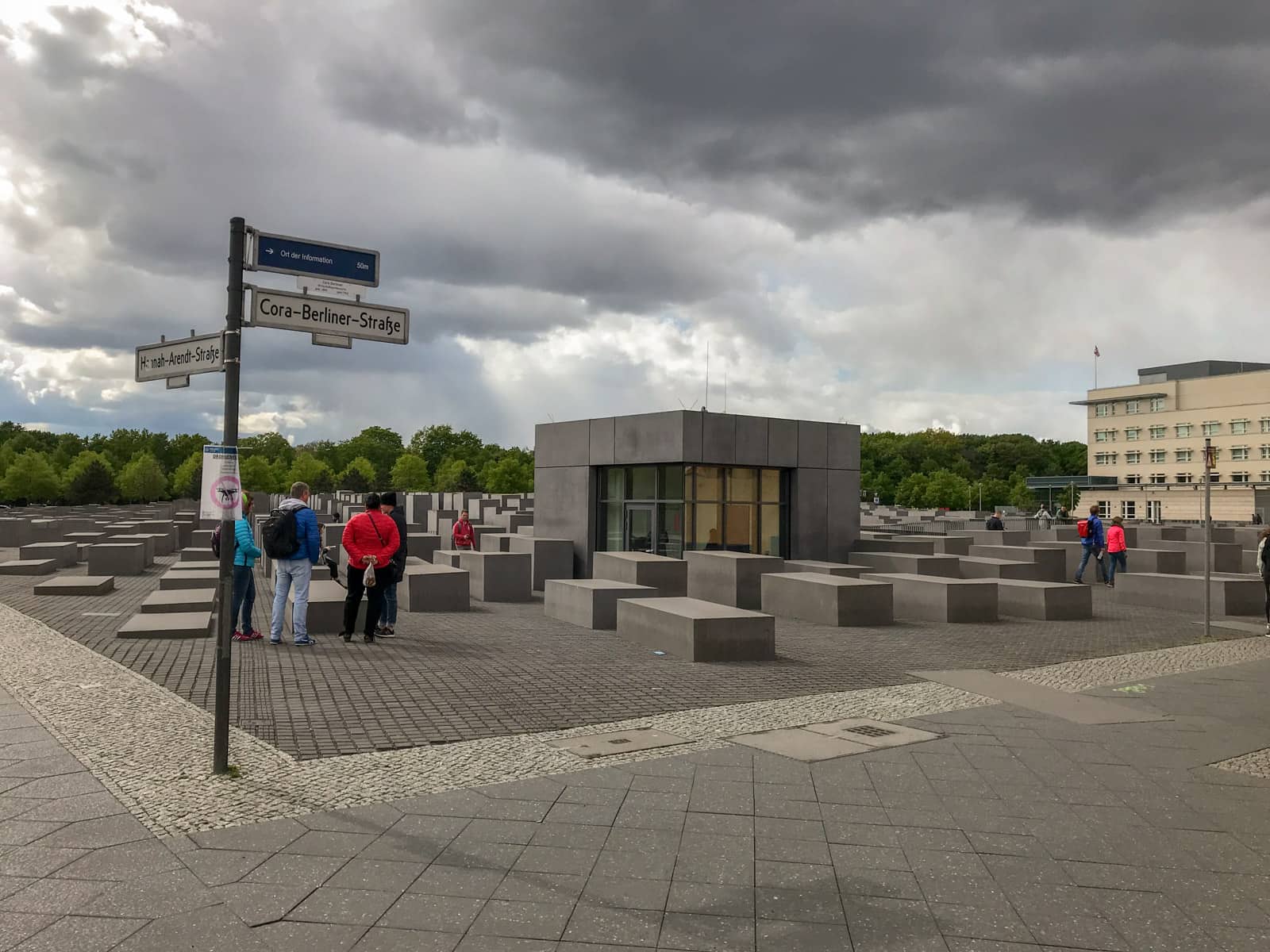 The outside of a memorial made from large rectangular pillars, as seen from the street. Amongst the pillars there is a small museum building that blends in with the pillars