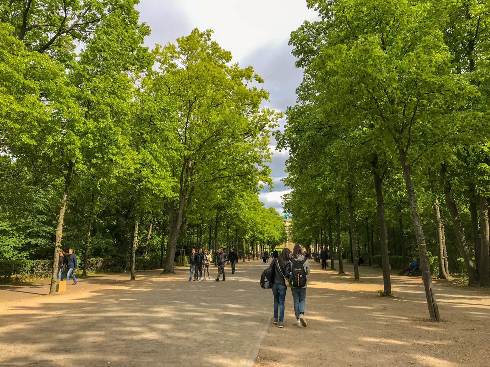 The inside of a park with stone paths laid out on the ground. There are some people walking and the sides of the path are surrounded with trees