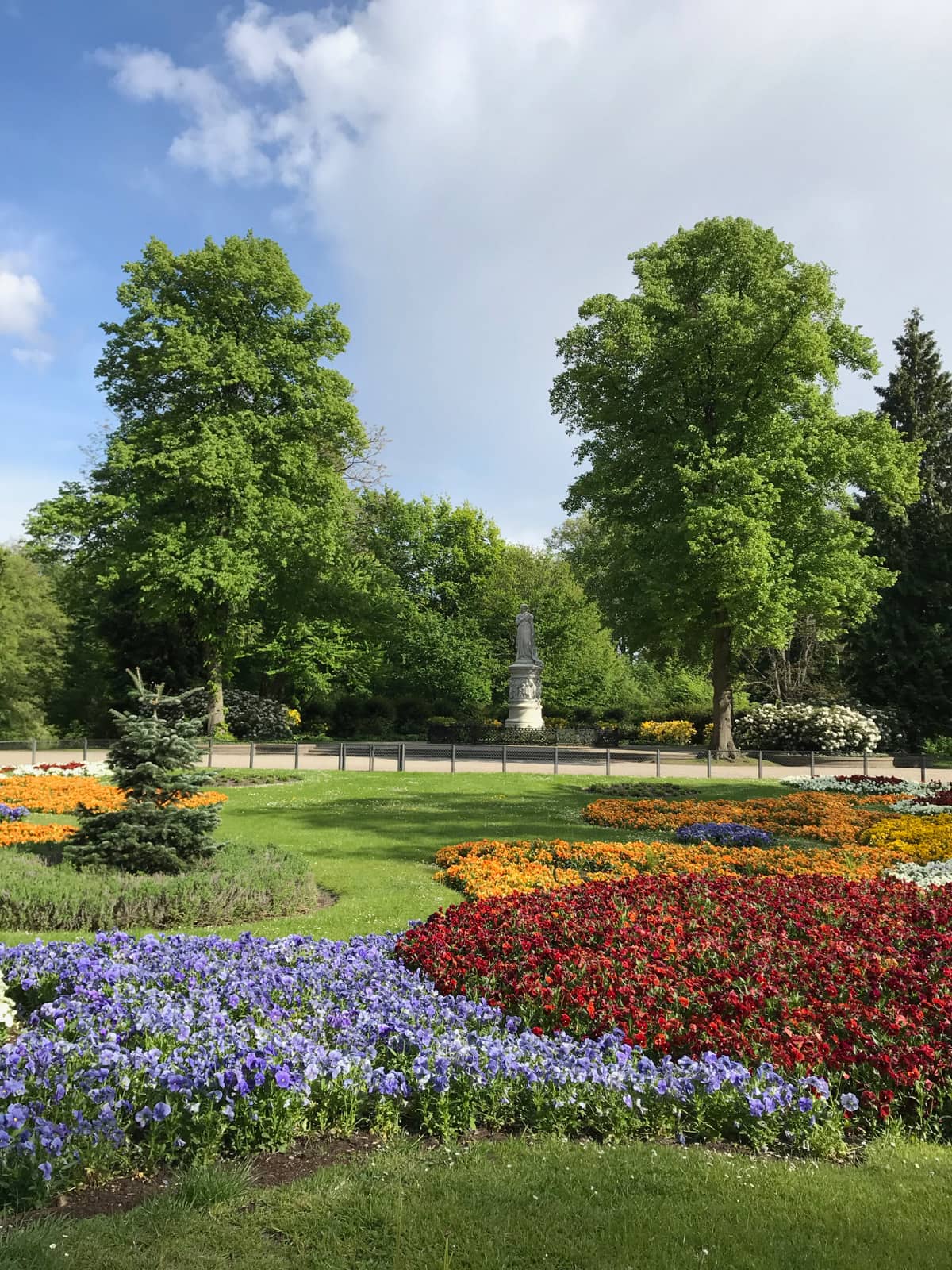The inside of a very green park with colourful flowers in the foreground and big trees in the background