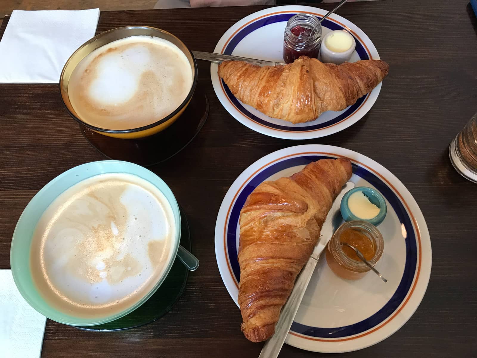 A table setting with two cups of coffee and two white plates with croissants and jam