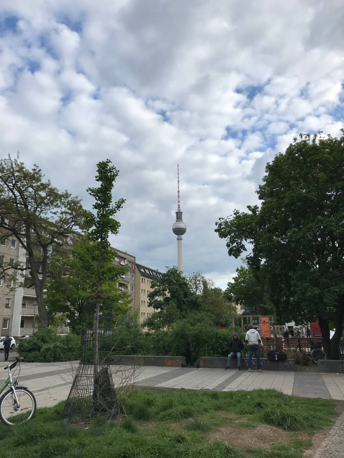 A small suburbian park, with both concrete and grass, and a television tower in the background