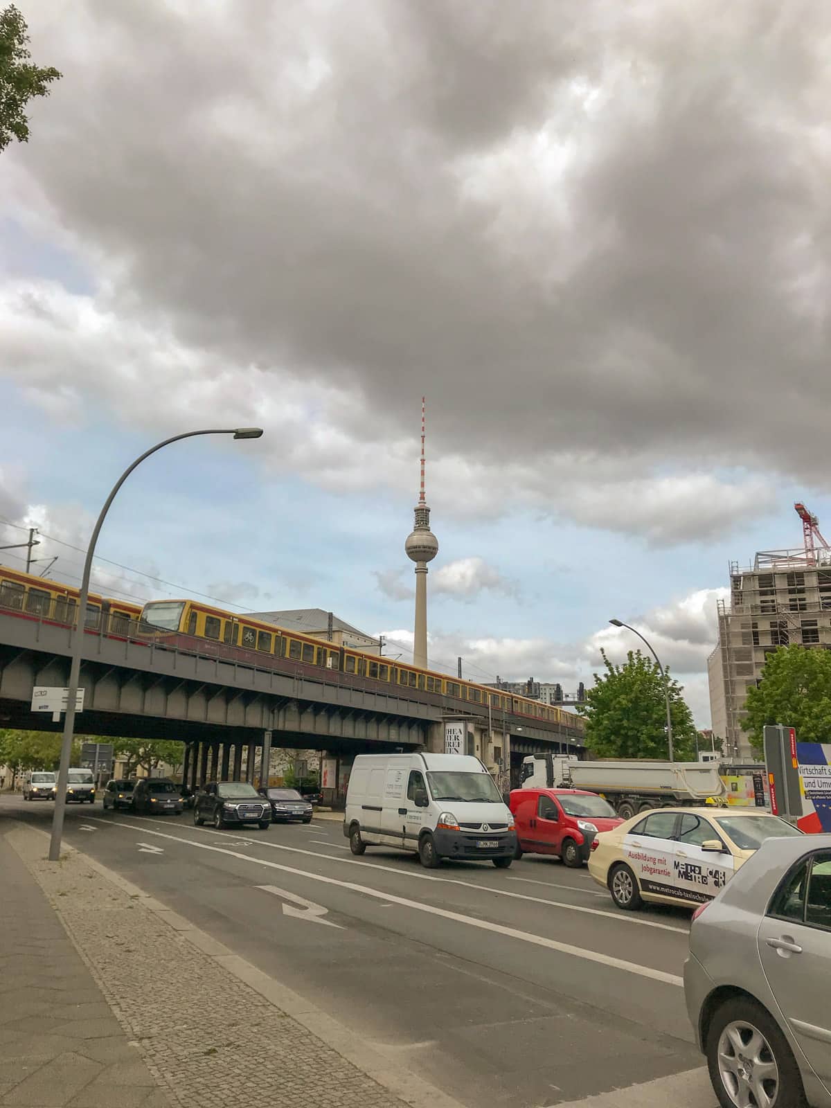 A view across a street with some cars on it, showing a train bridge in the background and a television tower further away. The sky is very cloudy