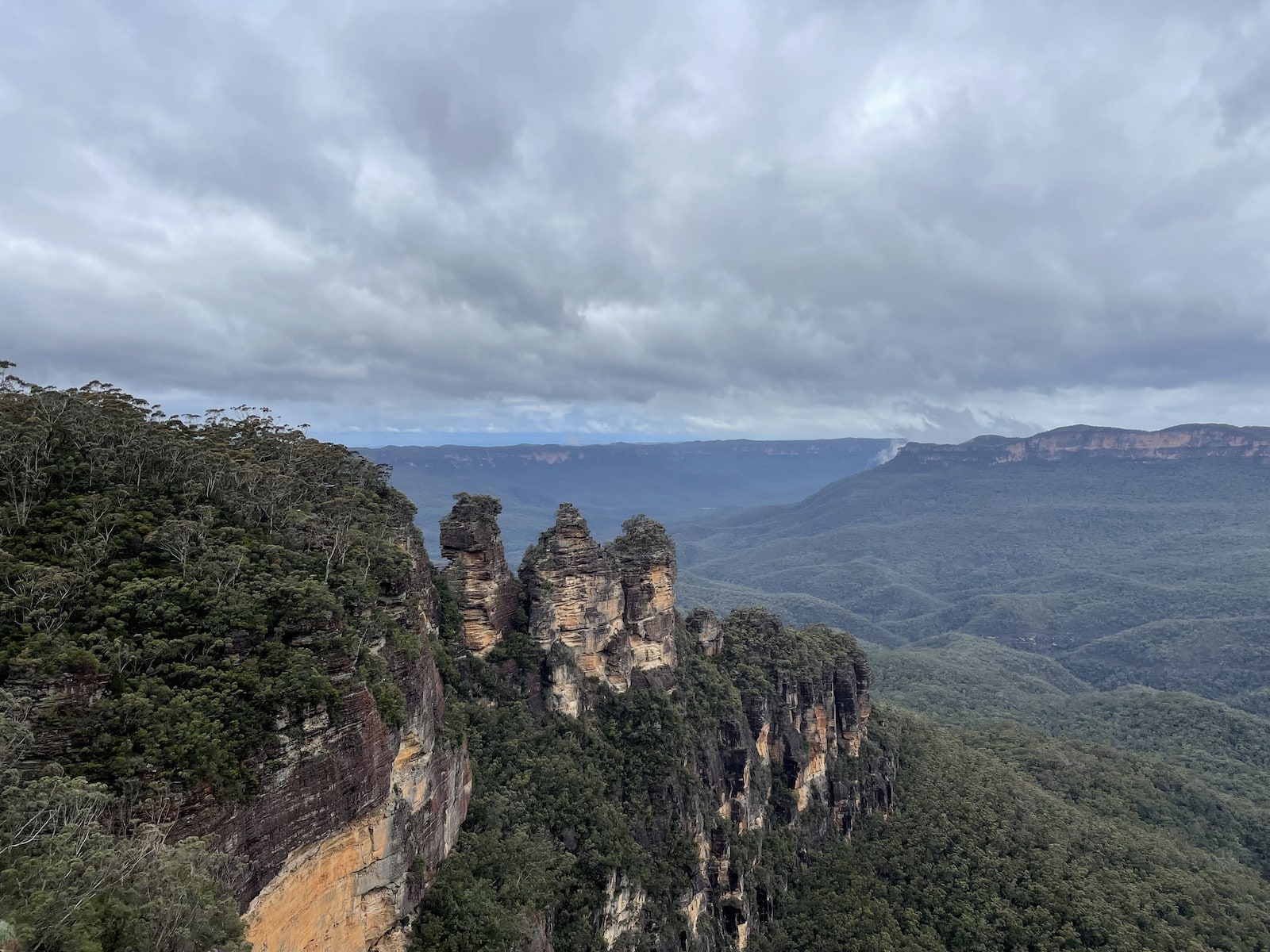 The Three Sisters in the Blue Mountains in Australia – three giant rock formations at the outset of mountain cliffs. The sky is cloudy