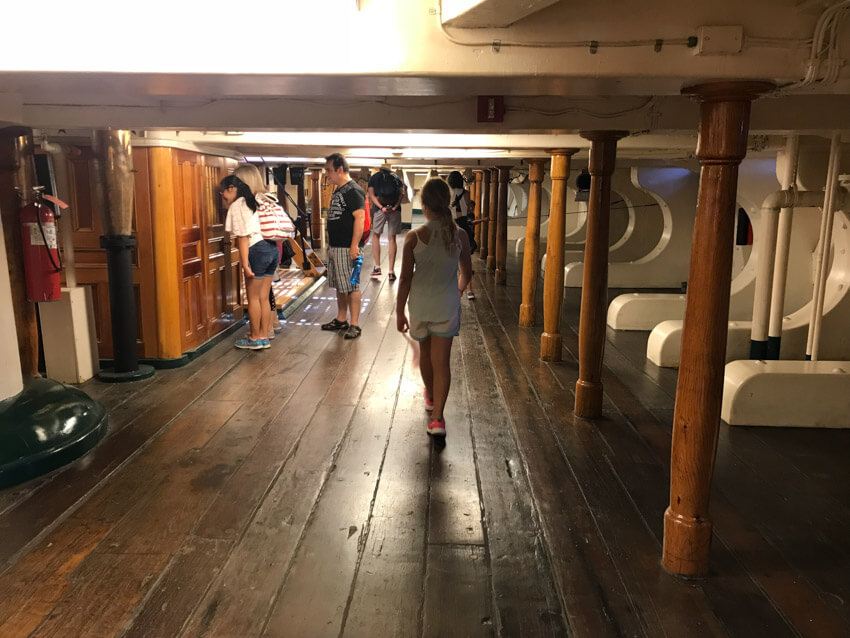 An area inside a ship with low ceilings. Some children and their parents are walking around with their necks bent to avoid hitting their head.