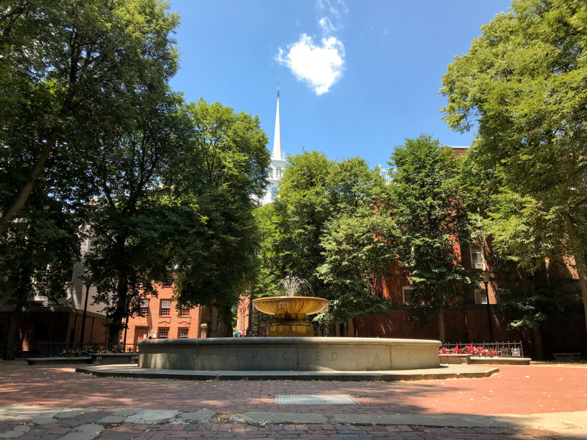 A shallow water fountain. In the background is a white chapel. The sky is very blue