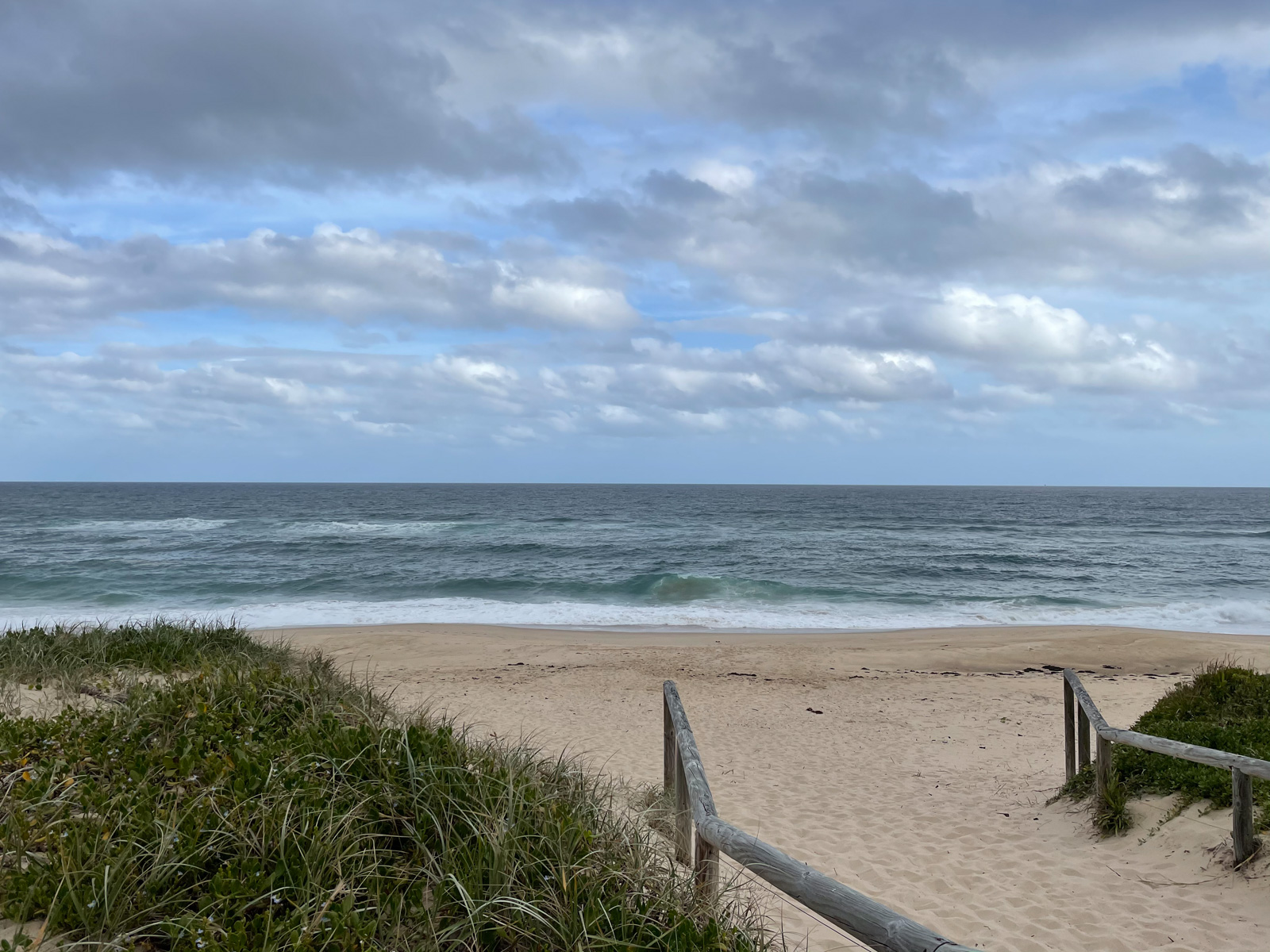 A beach in the afternoon. The sky is blue but has many grey clouds