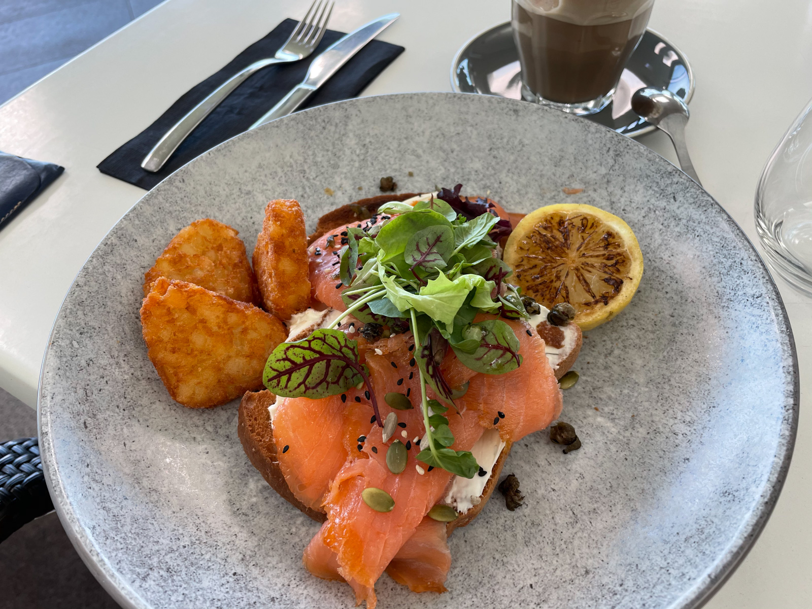 A grey plate with eggs on toast, with salmon and hash browns served on it