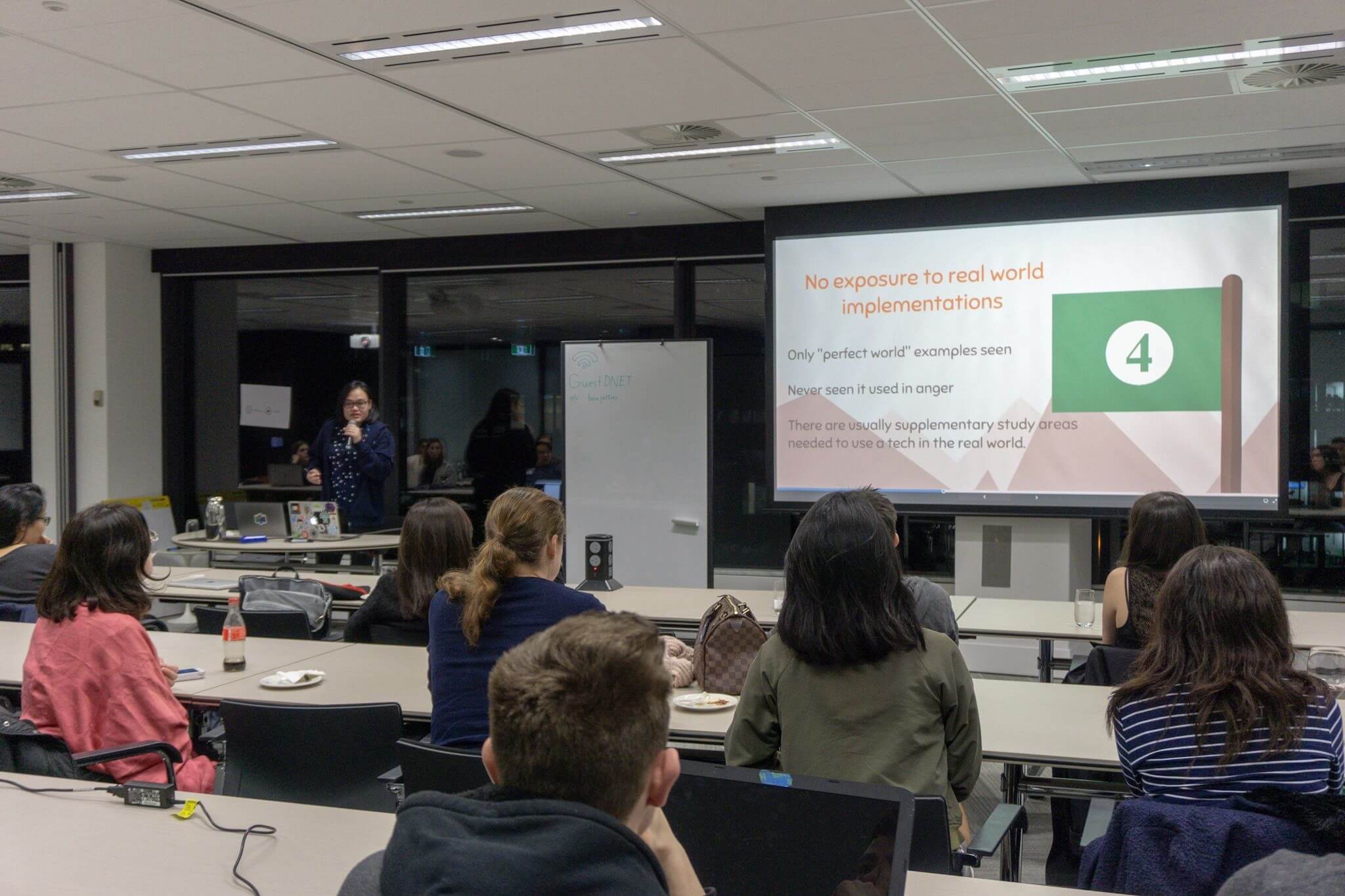 Similar setting to the other photos in this post, a different woman at the front of the room giving a presentation alongside large screens