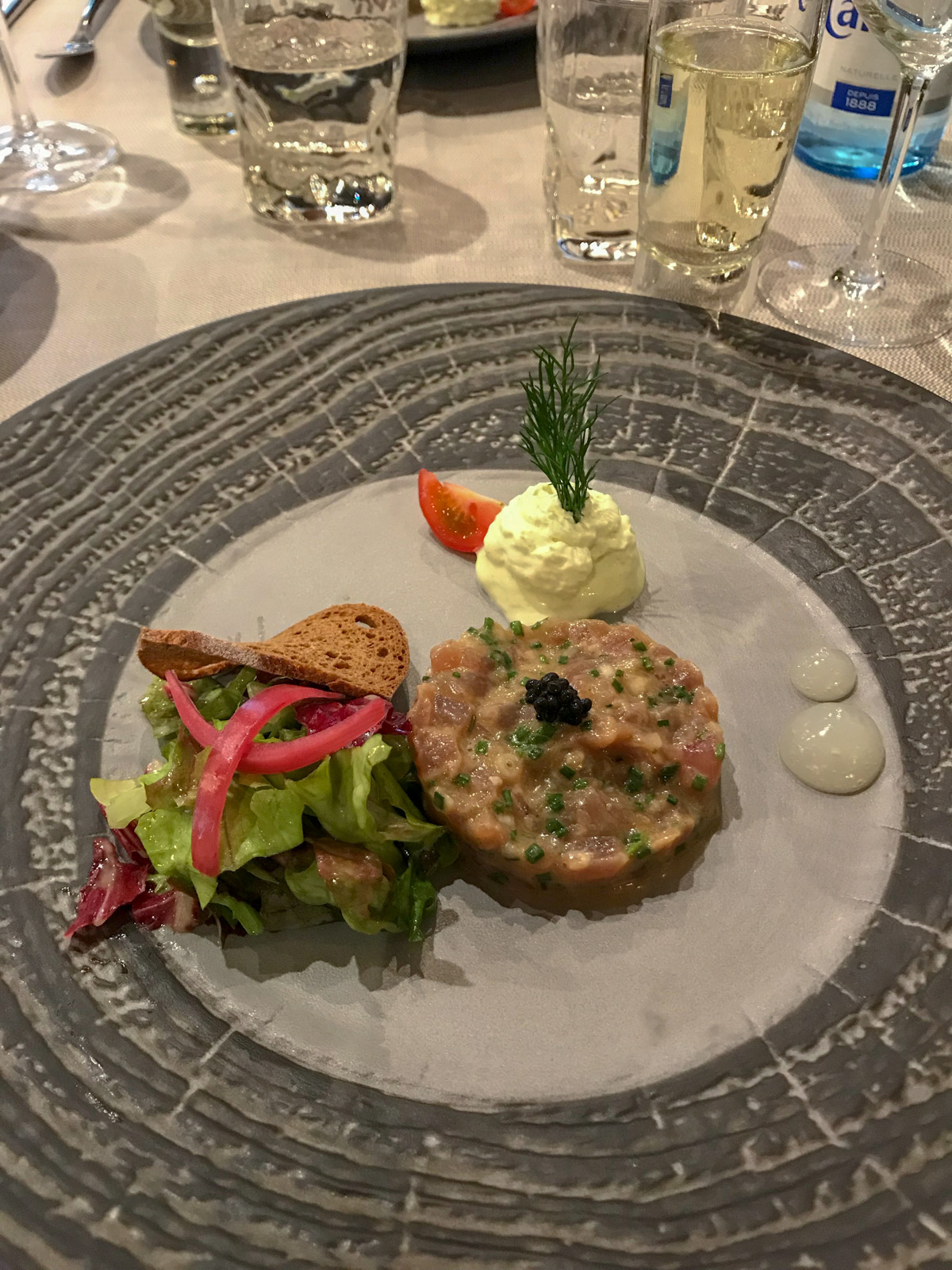 Raw tuna served with a small amount of salad and condiments, served on a grey plate with dark grey ridged patterns