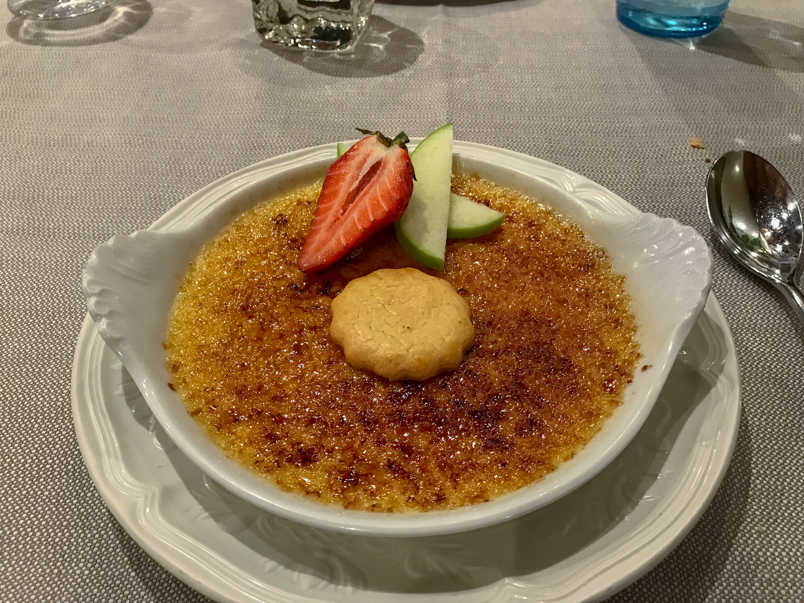 A white dish with creme brûlée served on it, topped with a couple of fruits