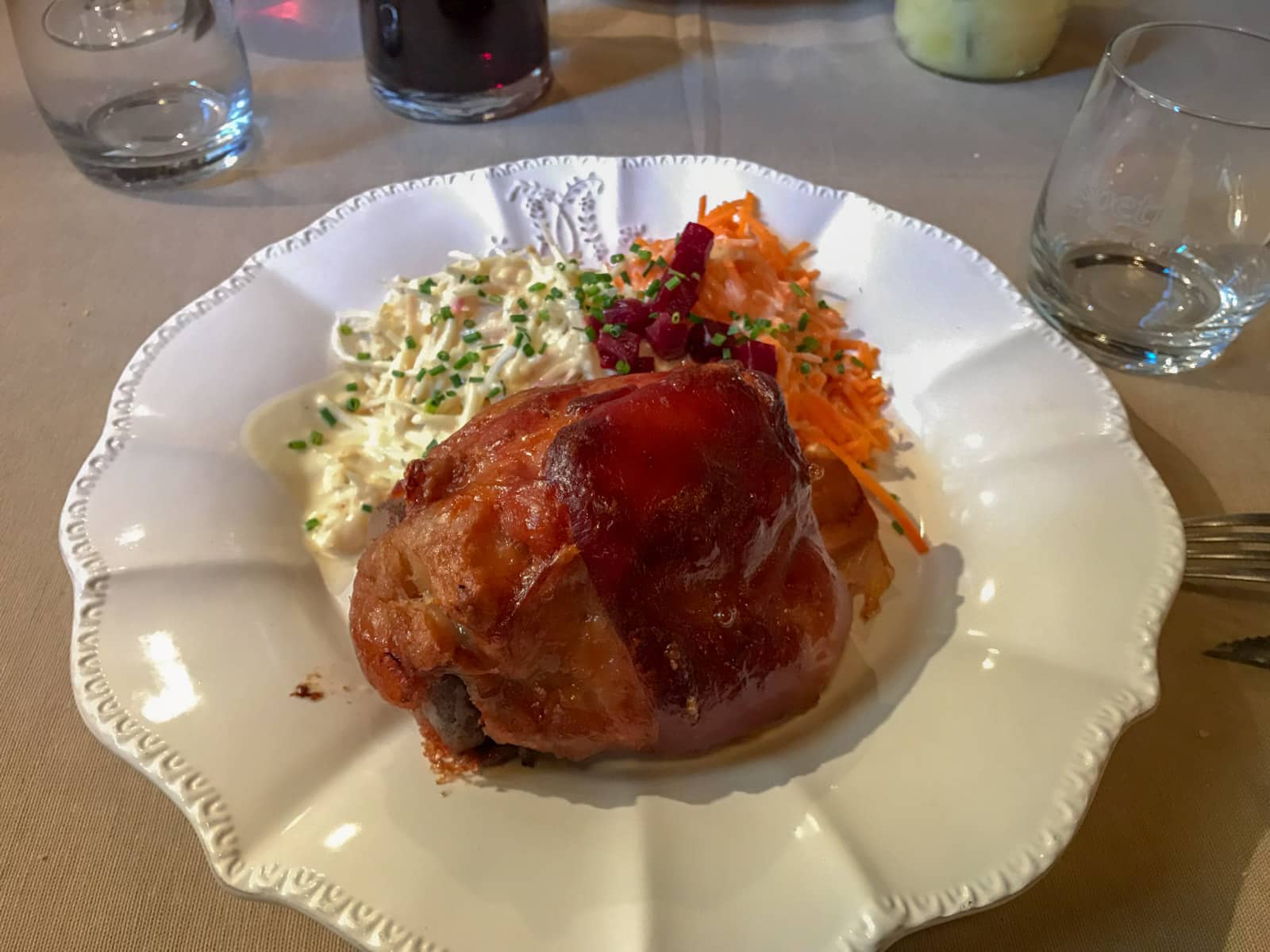 A white plate with pork knuckle and cabbage salad served on it