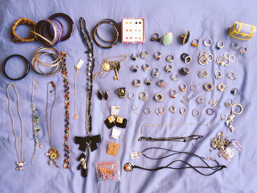 An assortment of necklaces, bangles and rings laid out on a light purple bedspread