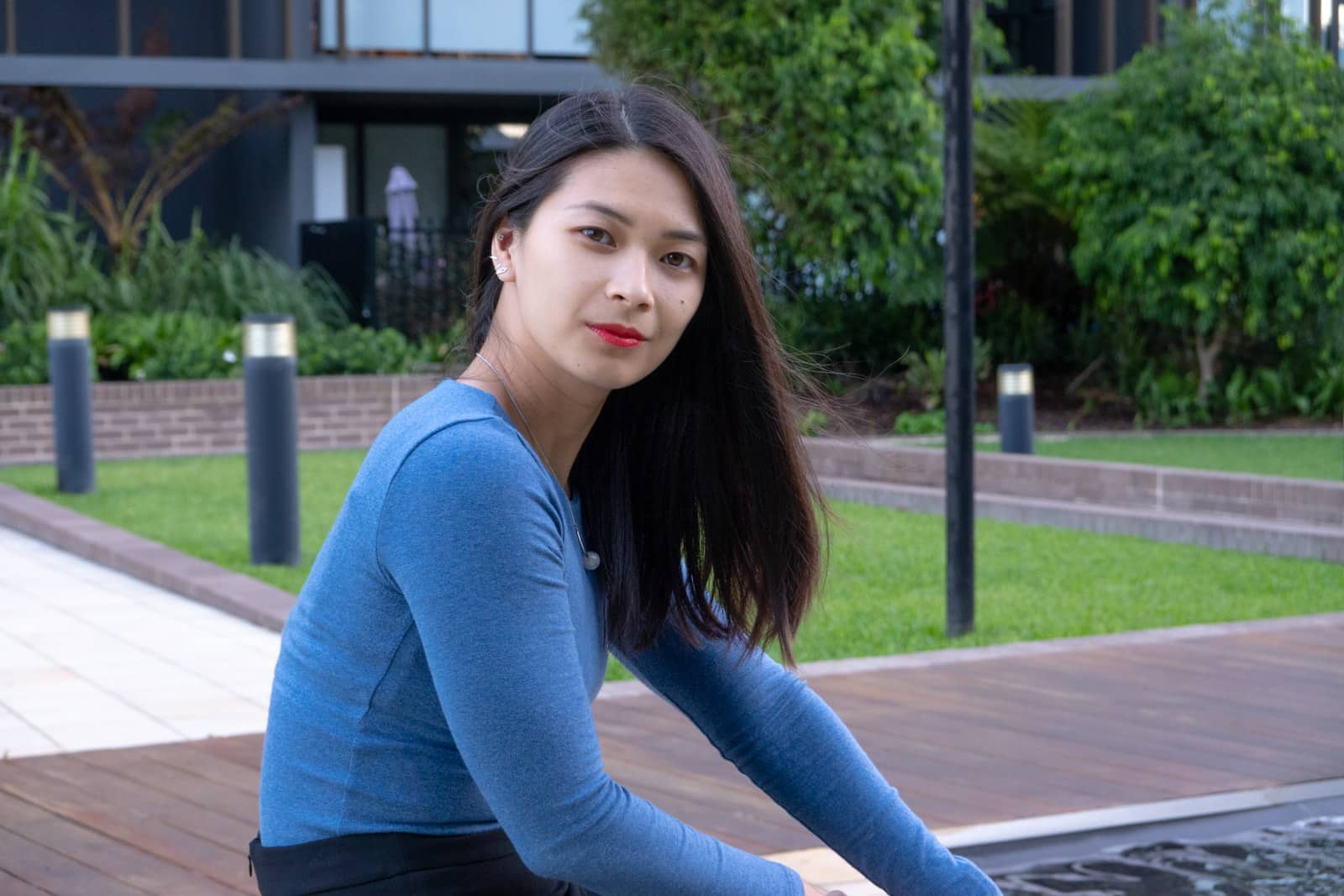 A medium shot of a woman with short dark hair, wearing a long-sleeved indigo blue top. She has bright red-orange lipstick on.