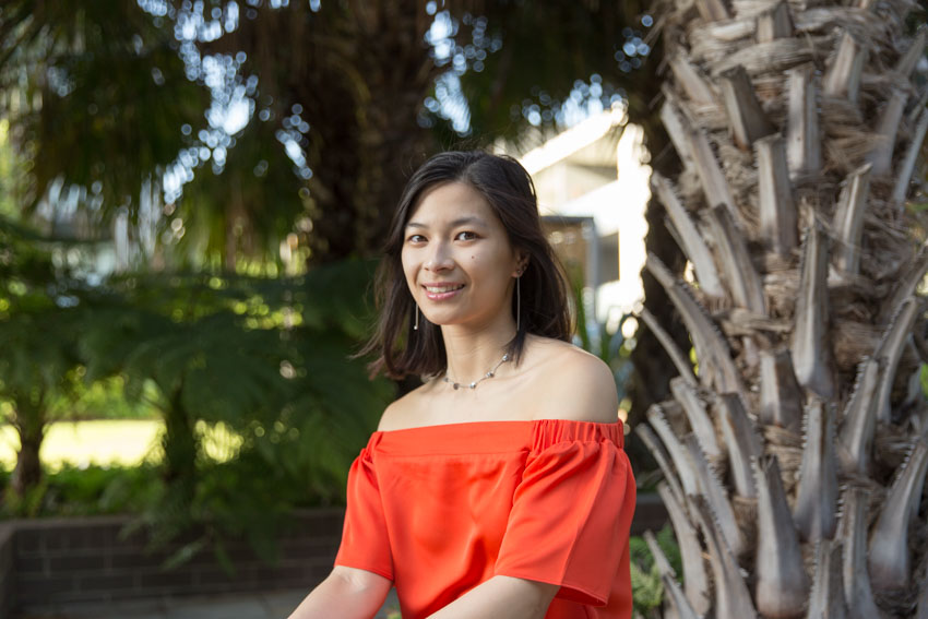 A girl with an orange top, smiling. Trees are in the background.