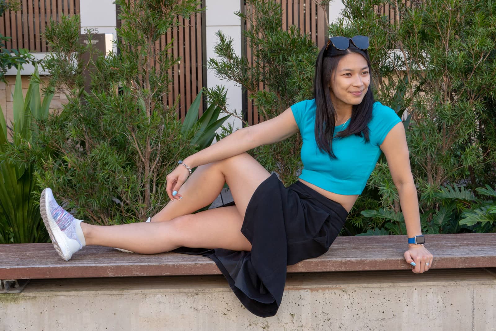 The same woman in other photos on this page, wearing the same outfit. She is sitting with her legs outstretched on a bench, one of them bent. She is smirking and looking away from the camera