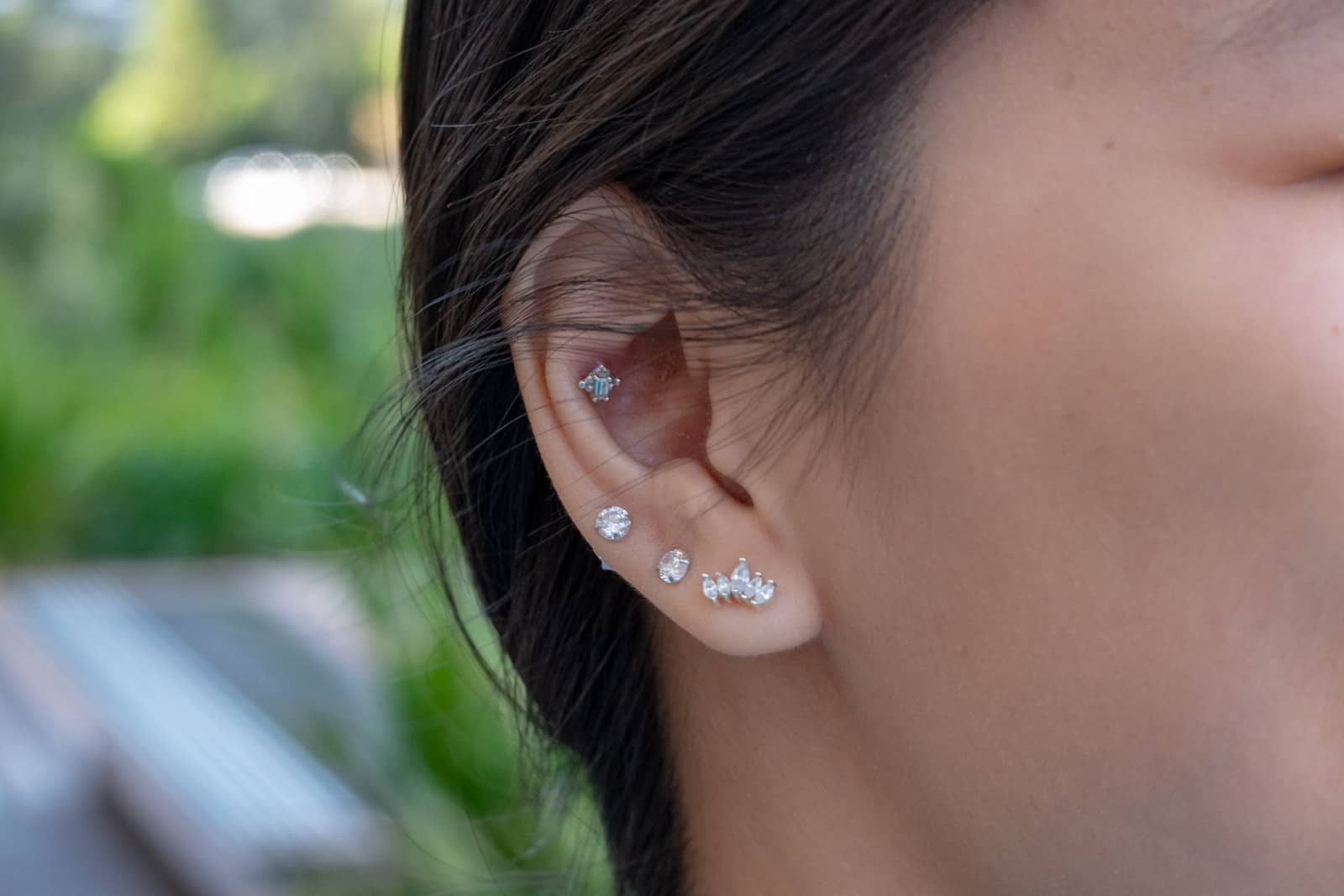 A close-up of a woman’s ear with three lobe piercings and one cartilage piercing. The bottommost piercing has a crown-shaped stud in it.