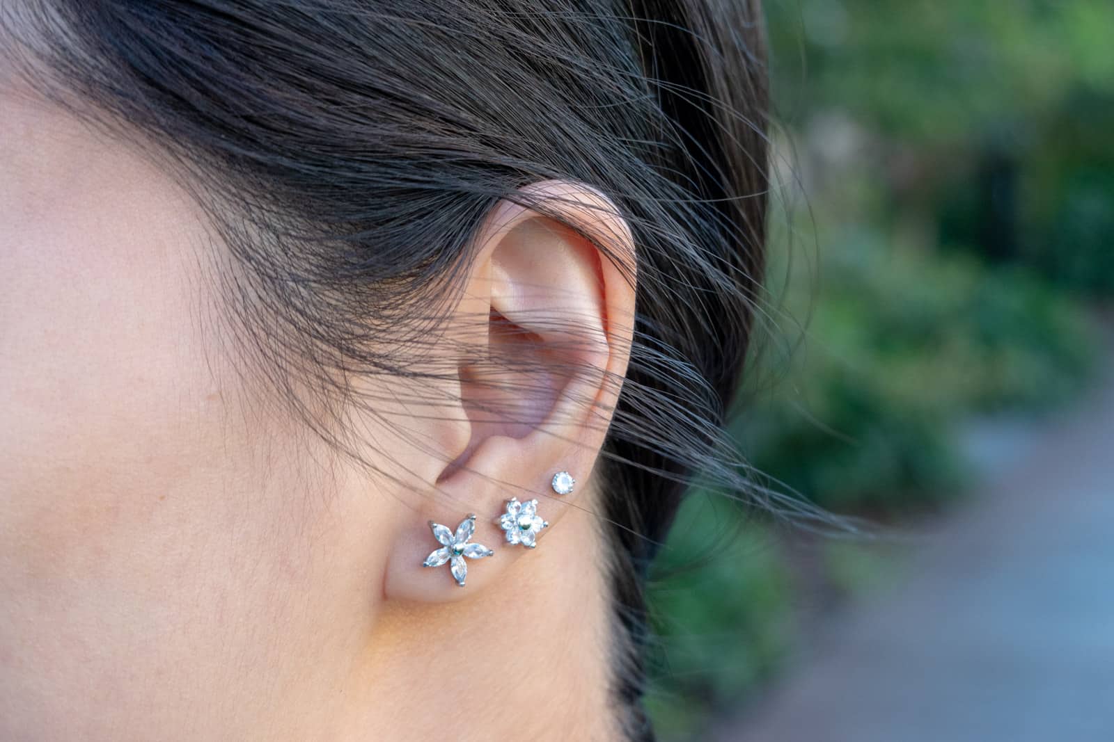 A close-up of a woman’s ear with three cubic zirconia studs studs in the lobe. Two of the studs resemble flowers and the other is a simple stud