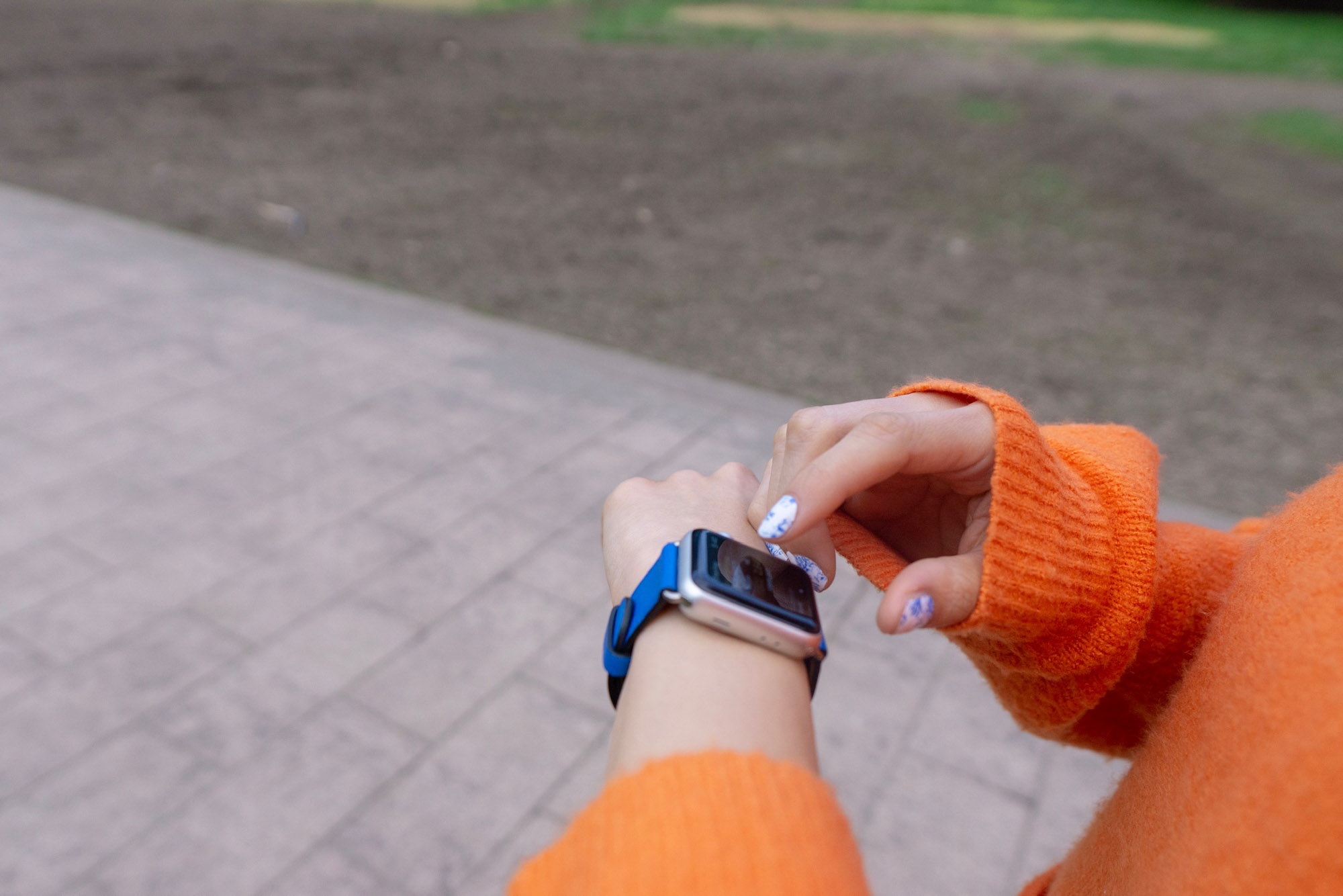 Close up of an Apple Watch on a woman’s wrist. The watch has a bright blue band. The woman is about to tap on the screen of the watch with her opposite hand.