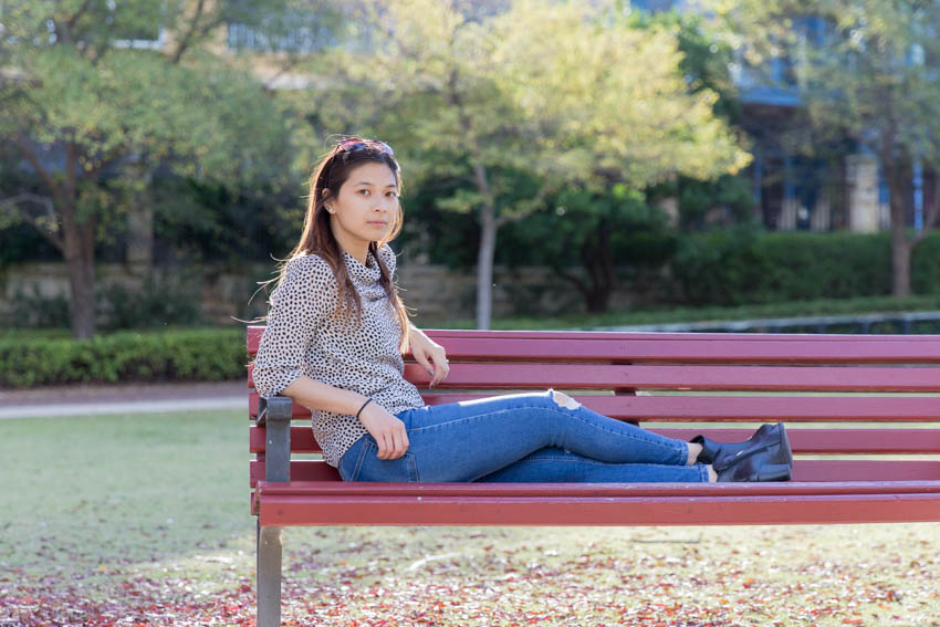 Me sitting sideways on a park bench with my legs on the bench and my arm resting on one of the arms