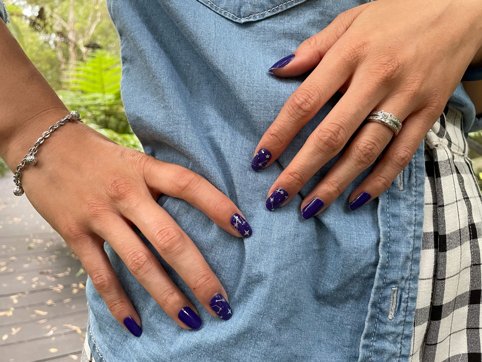 A close-up of a woman’s fingernails, with dark blue nail wraps applied. Some of the nails have a silver starry pattern on them.