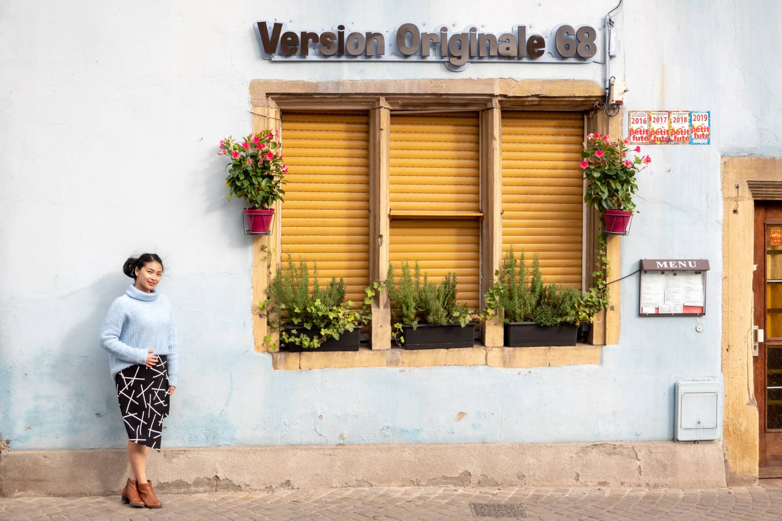 The same woman in other photos on this page, dressed in the same clothes. She is standing by the building with the wall that is light blue.