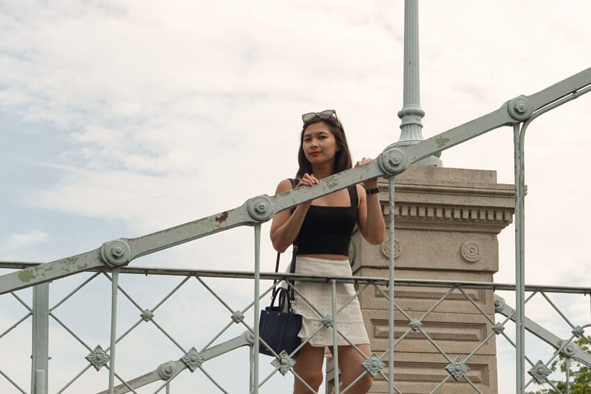 The same woman from the previous photo, standing on a bridge, with her hands resting on the railing.