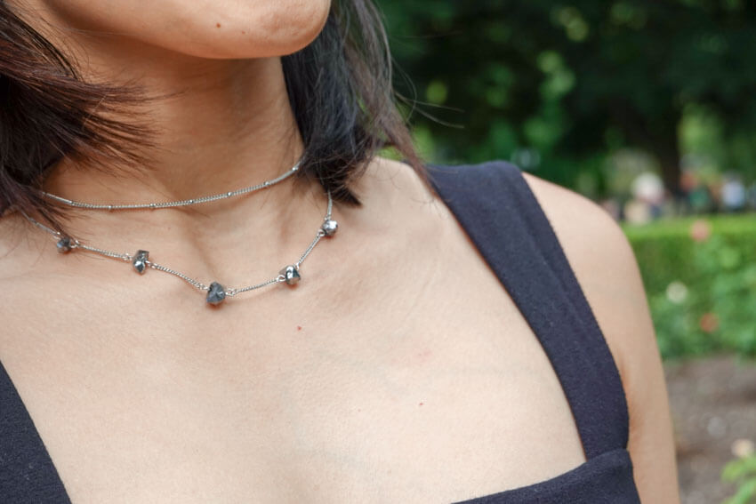 Close shot of a woman’s neckline, wearing two choker necklaces, one spaced with small silver rocks