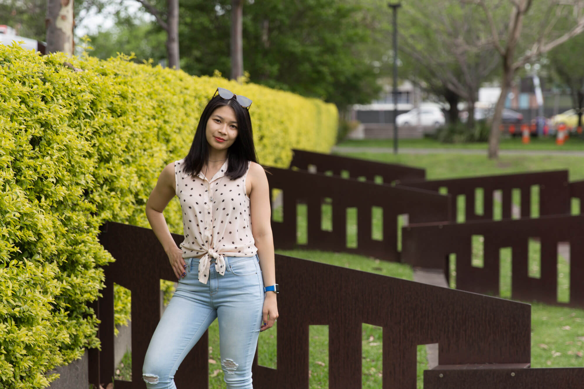 A woman standing in a park with short, dark brown angled metal fences behind her. She has a hand on her hip