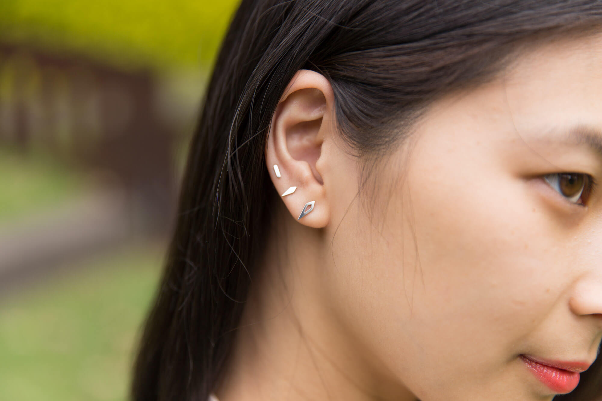 A closeup of the side of a woman’s face with the focus on three small silver earrings on her earlobe